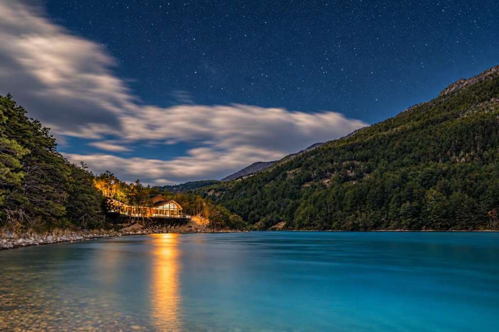 Patagonia Baker Lodge lit at night under the stars, reflected in the river