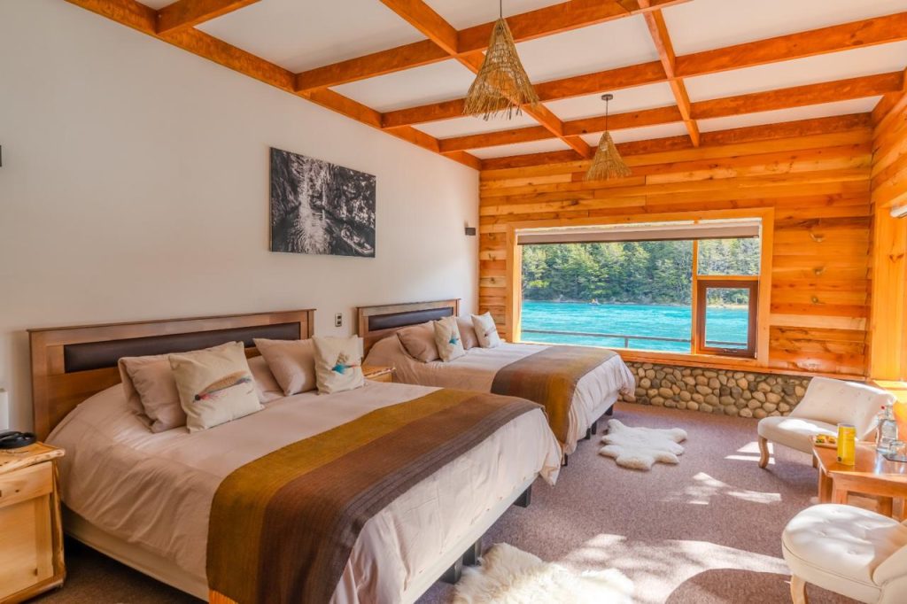 Guest room with two beds and a window over the turquoise Río Baker